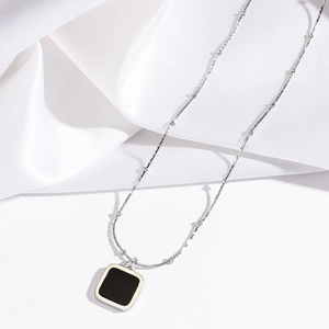 Detail of silver chain necklace with black square pendant on silk fabric background
