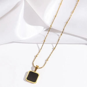 Close-up of gold bead chain necklace with a minimalist black square pendant on silk