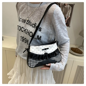 Detail of checkered shoulder bag with lace trim, bow, and heart pendant on a model