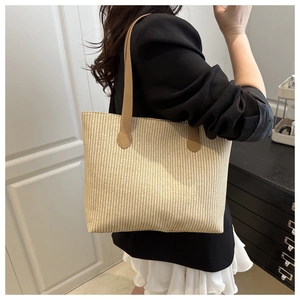 Detail of light beige woven tote bag with brown leather straps shown on a model