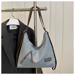 Detalle del bolso de mano tejido con diseño de espiga azul y blanco y correas de cuero marrón