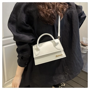 Détail d'un mini sac trapèze blanc avec logo doré et fine bandoulière amovible élégante