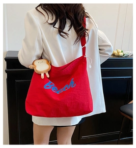Detail of red canvas tote bag with blue Beach lettering and cute plush bread charm decoration