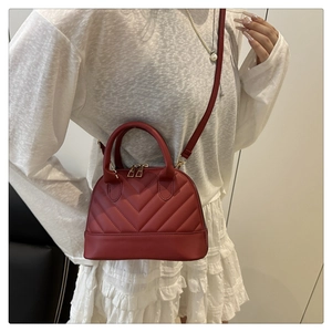 Sac dôme rouge matelassé avec détails dorés et bandoulière porté avec une jupe plissée