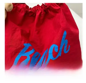 Detail view of red drawstring bag featuring blue Beach lettering on nylon fabric texture