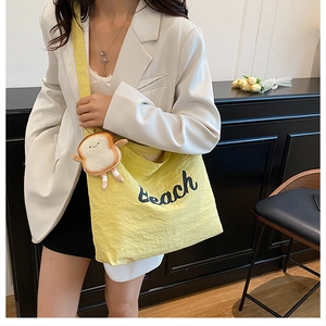 Detail of yellow canvas tote bag with Beach embroidery and plush toast charm on strap