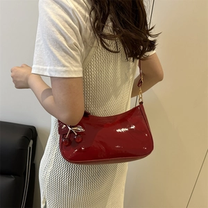 Sac à épaule en cuir verni rouge foncé avec breloque cerise porté par un mannequin