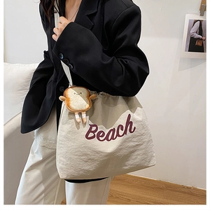 Λεπτομέρεια της off-white πάνινης τσάντας με μοβ κείμενο Beach και λούτρινο κρεμαστό τοστ
