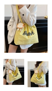 Detail of a bright yellow tote bag with Beach lettering and a cute bread plush charm