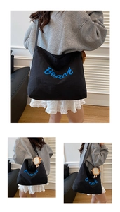Detail of black canvas tote bag with blue Beach embroidery and cute plush pendant