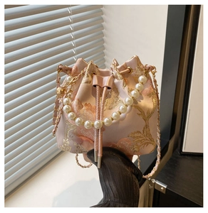 Detail of pink satin bucket bag featuring gold floral embroidery and pearl handle accent