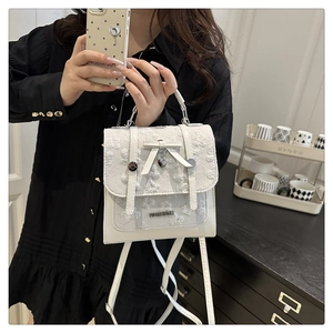 Détail du sac à bandoulière blanc avec motif nœud et pendentif cœur dans un salon
