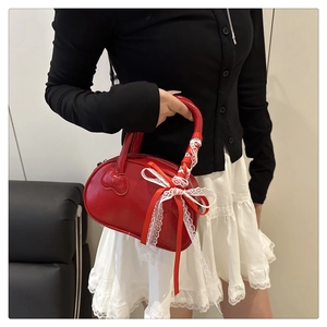 Detail of red patent leather handbag featuring white lace bow and cat face embossing