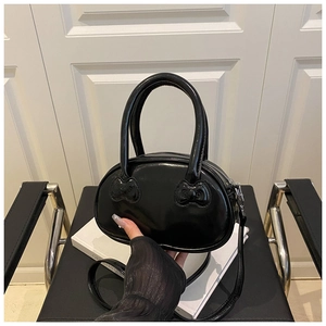 Detail of black glossy handbag with iconic dual bow embossed pattern and twin handles