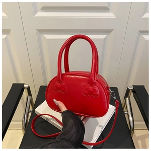 Detail of red faux leather handbag featuring a unique embossed bow on the handle attachment