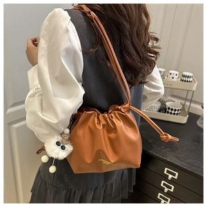 Detail of caramel pleated bucket bag featuring drawstring closure and plush monster charm