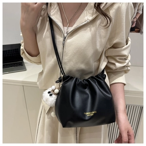 Close-up of black pleated cloud bag with drawstring and white plush pendant detail