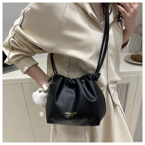 Detail of black pleated bucket bag with gold lettering, white pompom and cute charm