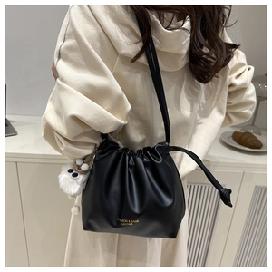 Detail of black leather drawstring bucket bag with plush charm on a casual outfit