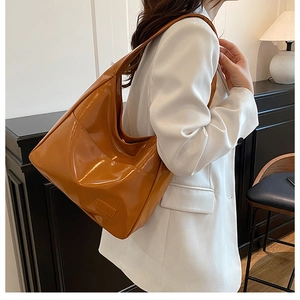 Detailed view of caramel glossy leather hobo bag worn over the shoulder in a minimalist room