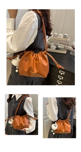 Detail of a brown drawstring bucket bag featuring a white plush charm and leather strap