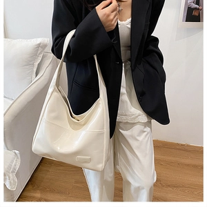 Detail of a large white glossy tote bag worn by a model in a minimalist home setting