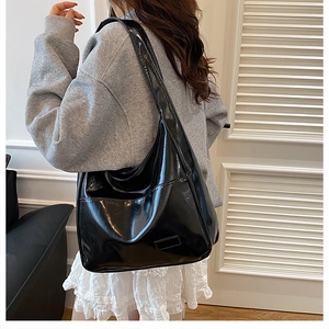 Close-up of black high-gloss leather tote bag with side pocket shown on a model