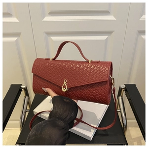 Close-up of burgundy woven leather bag featuring a gold infinity buckle and flap cover