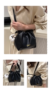 Detail view of black pleated bucket bag with plush charm and golden logo lettering