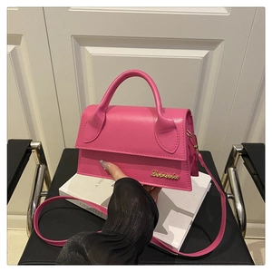 Détail du mini sac en cuir fuchsia avec logo doré et bandoulière sur une chaise en cuir