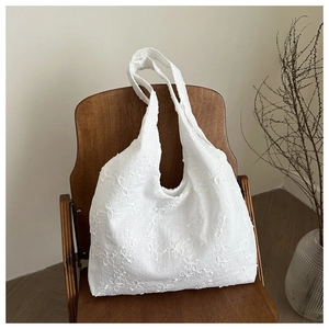 Detailed view of white canvas tote bag with floral embroidery and long shoulder straps