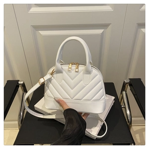 Detail of white quilted shell-shaped handbag with V-shaped stitching and golden zipper