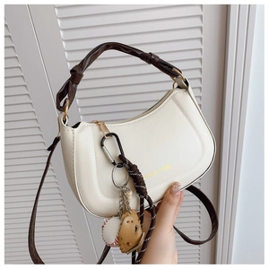 Detail of cream half-moon bag with knotted brown handle and baseball glove charm decor