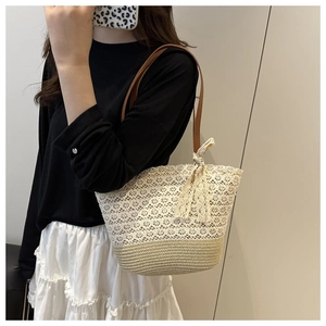 Detail of hollow woven straw tote with lace bow charm and premium leather strap