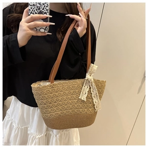 Detail of woven straw tote bag featuring white lace bow and brown leather shoulder strap