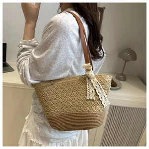 Detail of hollow woven straw tote bag with brown leather strap and white lace bow