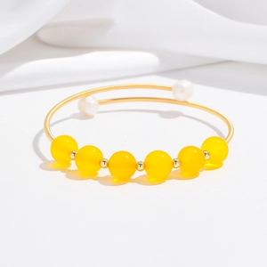 Dettaglio del bracciale aperto in oro con perle gialle e bianche su seta bianca