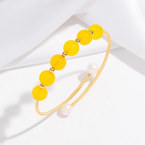 Bracciale rigido dorato con perle di agata gialla e perle su sfondo bianco pulito