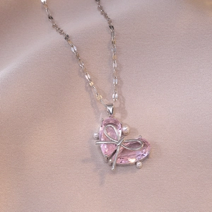 Collier avec pendentif cœur rose, nœud argenté et perles sur tissu rose élégant