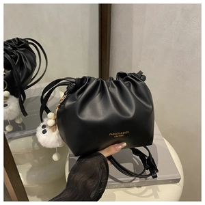 Detail of black pleated bucket bag with gold lettering and cute white plush charm