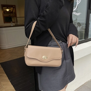 Minimalist beige crossbody bag with gold twist lock shown on model in a modern café setting