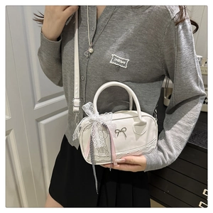 Close-up of white bowling bag featuring lace trim, metal bow logo, and ribbon charms