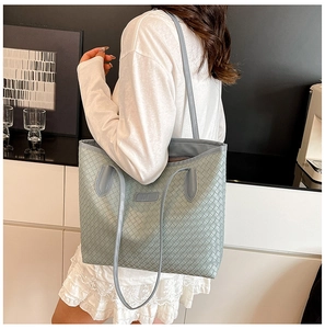 Close-up of a sage green woven tote bag with premium leather texture on a female shoulder