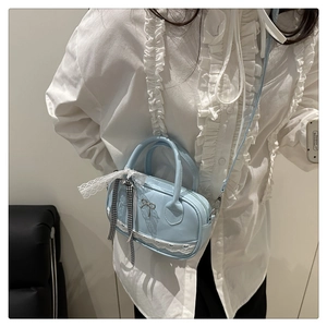 Light blue mini shell bag with lace trim and bow charm worn by a model in white