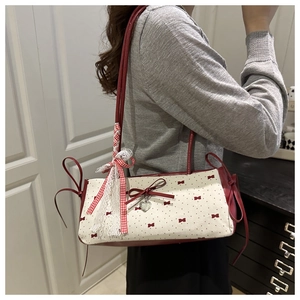 Detail of red bow prints and silver heart pendant on a white canvas shoulder bag