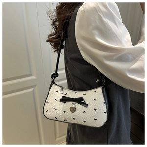 Detail of white jacquard underarm bag with black bow and heart-shaped metal pendant