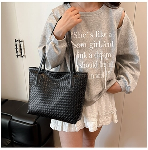 Detail of classic black woven faux leather tote bag shown in a cozy indoor setting