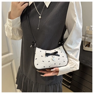 Détail du sac croissant texturé blanc avec motifs nœuds noirs et pendentif cœur
