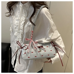Detail of light blue crossbody bag with 3D red bows and heart charm worn by model