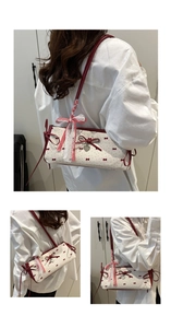 Detail of a creamy white rectangular handbag with red bows and a heart pendant charm